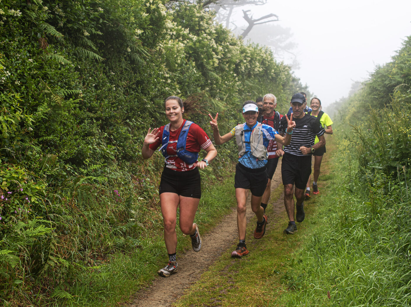 Un groupe de coureuses et coureurs souriants sur le sentier du GR34 dans la brume, à Déolen